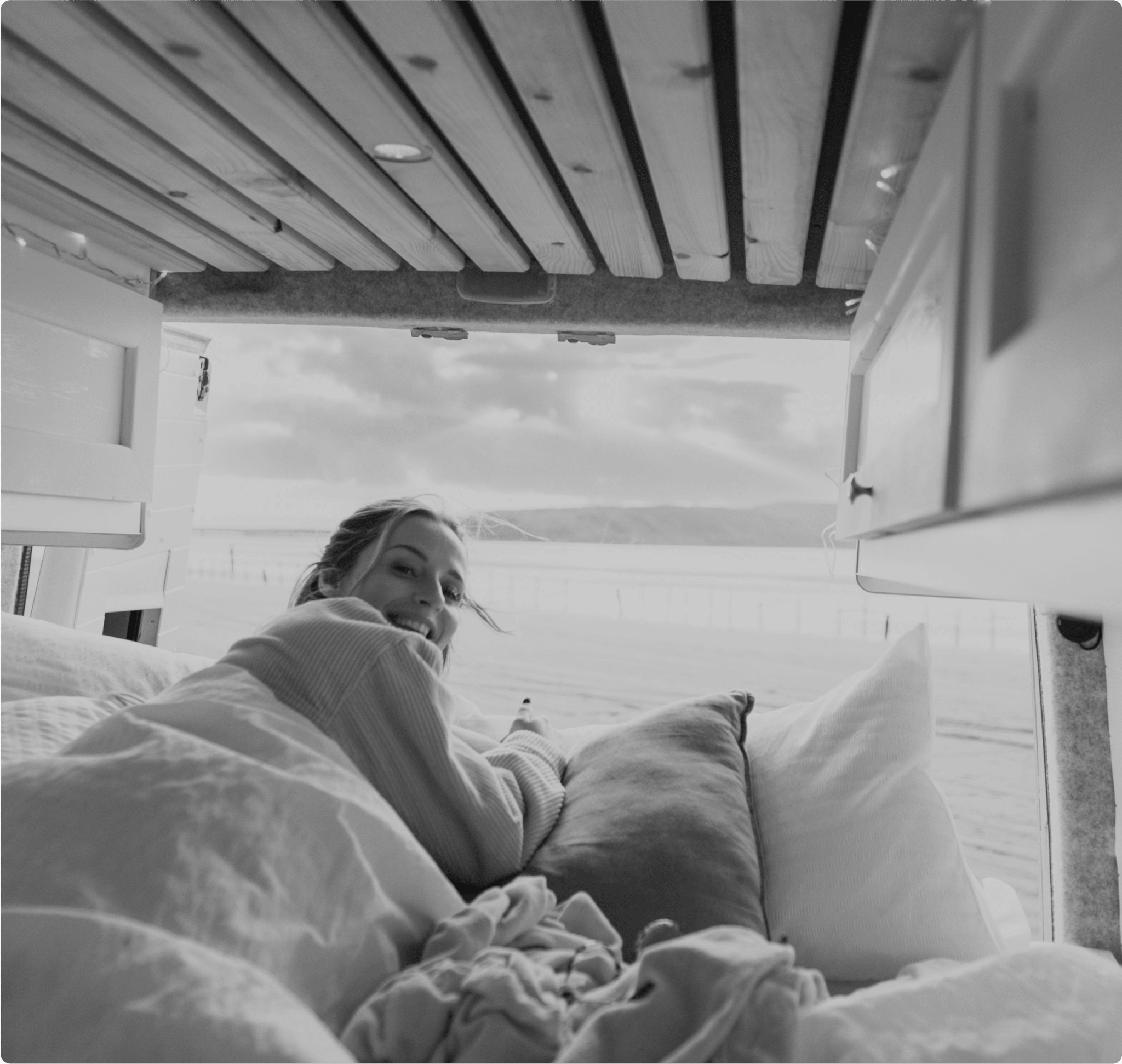 Une femme qui se lève au bord de mer dans sont lit avec les portes du van ouverte